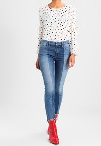 Blusa bianca con pois neri, maniche lunghe. Jeans skinny in denim blu, lavaggio chiaro a medio. Stivaletti alla caviglia in pelle rossa lucida.