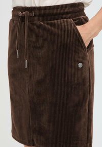 Jupe en velours côtelé marron avec des nervures verticales, dotée d'une taille à cordon de serrage, de poches latérales et d'un petit accent de logo en métal.