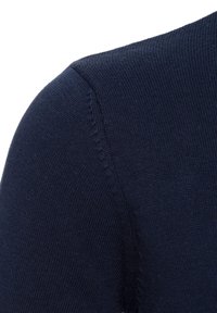 Gros plan sur l'épaule d'un pull en maille bleu marine montrant la texture du tissu et le détail de la couture.