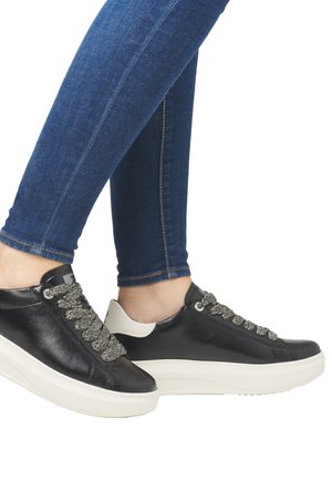 Baskets en cuir noir avec des lacets gris texturés, des accents blancs et une épaisse semelle blanche. Portées avec un jean bleu ajusté.