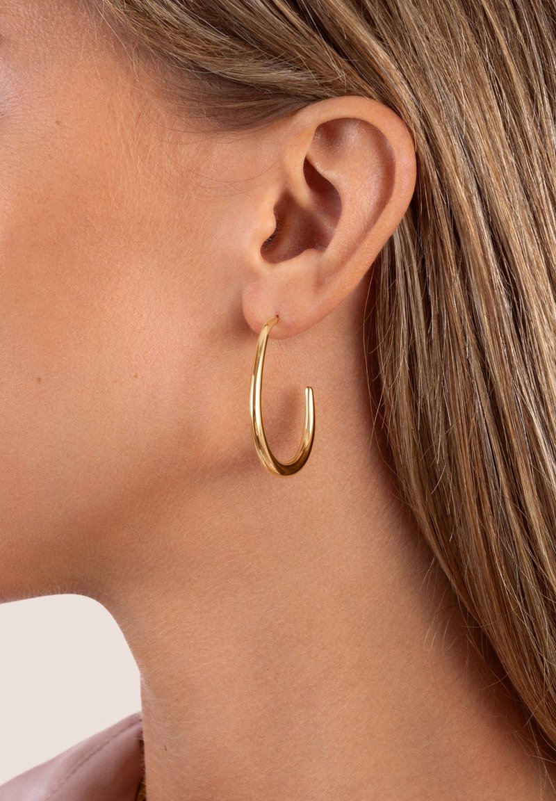 Guld hoopörhänge med en elegant, böjd design. Slät yta med en blank yta, som visar en avlång tårform.