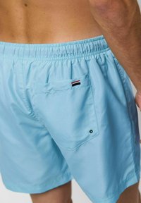 Svetlo modre kopalne hlače iz gladkega materiala, z elastičnim pasom, zadnjim žepom z obrobami in zaponko na pritrditev.