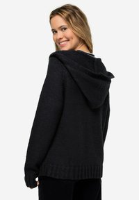 Felpa con cappuccio nera, caratterizzata da un design lavorato a maglia testurizzata, vestibilità ampia e orlo a coste. La parte posteriore presenta un collo semplice e dettagli di cucitura sottili.