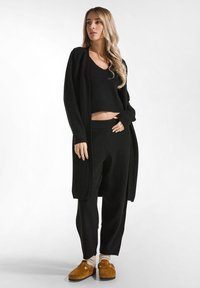 Zwarte gebreide set bestaande uit een cropped V-hals top, wijde broek en een lange cardigan. Gepaard met bruin suède instappers en crèmekleurige sokken.