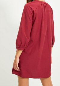 Rotes Baumwollkleid mit lockerer Passform, 3/4 Puffärmeln und einer gerafften Ausschnittdetail. Glatte Textur und Länge über dem Knie.