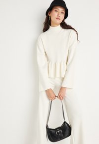 Top bianco a maniche lunghe con collo alto e maniche svasate, dotato di un orlo peplum. Abbinato a pantaloni bianchi e una borsa nera con dettaglio a fibbia.