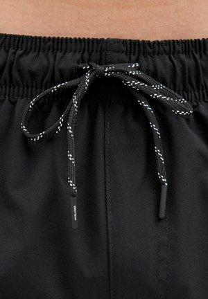 Schwarze Badeshorts mit einem gerafften Bund und schwarzem Kordelzug mit weißen Akzenten. Glatte Textur, minimalistisches Design, keine sichtbaren Muster.