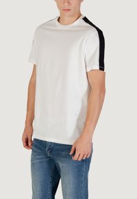 T-shirt bianco in cotone con dettagli neri sulle spalle, scollatura tonda e maniche corte. Tessuto morbido con una vestibilità comoda.