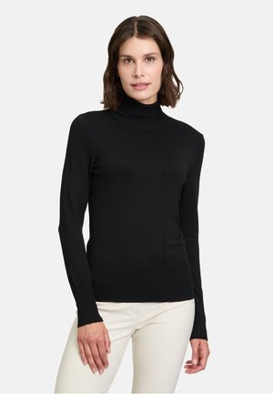 Black turtleneck sweater with long sleeves, slim fit, ribbed neckline and cuffs, paired with light-colored pants. Smooth, knitted texture.