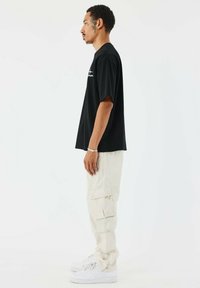 Camiseta negra de manga corta con un ajuste holgado, combinada con pantalones cargo beige claros. Zapatillas blancas completan el atuendo.