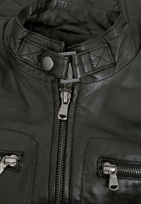Schwarze Lederjacke mit hohem Kragen, ausgestattet mit mehreren Reißverschlüssen und gesteppten Details. Glatte Textur mit Metallakzenten und Nähten.