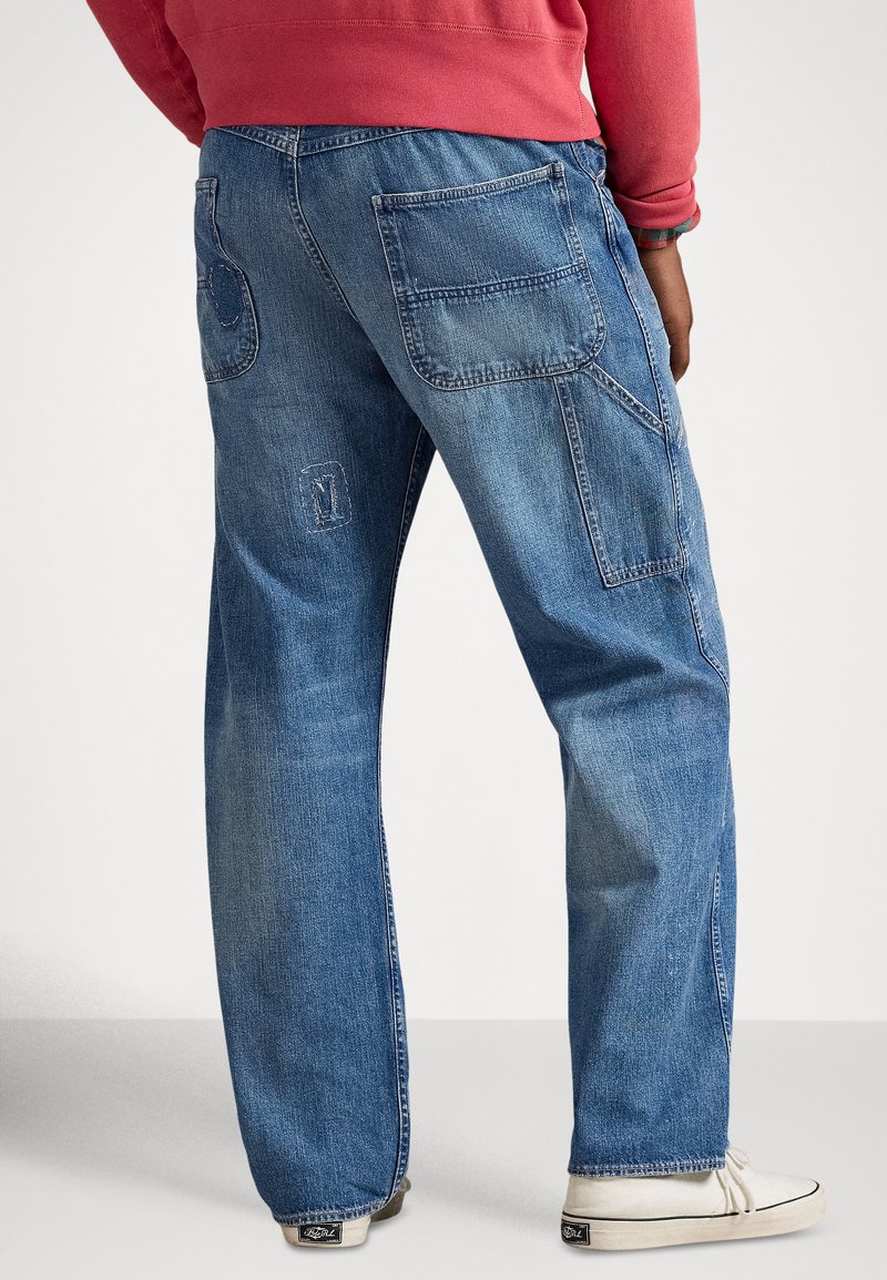 I pantaloni cargo in denim blu presentano molte tasche, una vestibilità comoda e una texture slavata. La cucitura posteriore include un accento decorativo a motivo.