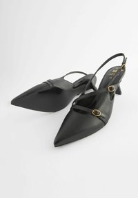 Musta nahkainen slingback-korkokenkä, jossa on terävä kärki, ristiin menevät hihnat ja kultaisentyyppiset yksityiskohdat. Korko on keskipitkä ja pohja on teksturoitu.