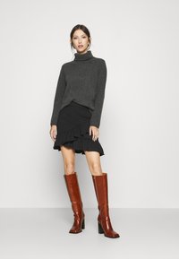 Suéter de gola alta cinza escuro, saia preta com babados e botas altas de couro castanho com salto, com um acabamento brilhante. Design simples e elegantes.