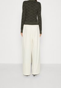 Grüner Pulli mit geometrischem Muster, kombiniert mit hoch taillierten, weit geschnittenen weißen Hosen mit Gesäßtaschen und lockerem Schnitt.