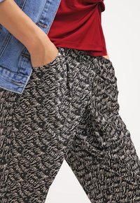 Mustat housut, joissa on kaikkialla valkoinen käsinkirjoitettu tekstikuosi, rento malli ja taskut, yhdistettynä punaiseen paitaan ja farkkutakkiin.