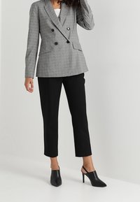 Blazer à carreaux gris croisé avec boutons noirs, assorti à un pantalon noir fuselé et des escarpins slingback noirs. Texture lisse.