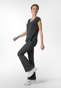 T-shirt nero a collo a V con maniche corte, abbinato a pantaloni svasati grigio scuro. Sneakers chiare con dettagli in rete completano l'outfit.