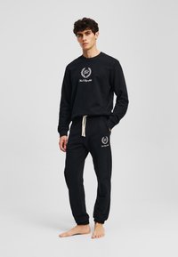 Set de hanorac și pantaloni de jogging negri, realizat dintr-un material moale. Prezintă un logo brodat și o talie cu șnur. Manșete fixate la glezne.
