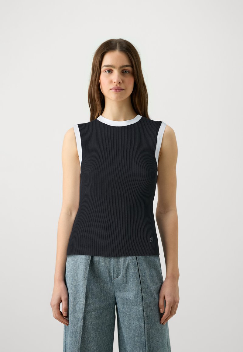 Αμάνικο, εφαρμοστό τοπ σε σκούρο ριμπ ύφασμα με λευκό ρεγκλάν λαιμό. Διαθέτει μια διακριτική λογότυπο στο στρίφωμα. Συνδυάζεται με ανοιχτό μπλε παντελόνι σε ευρύ κόψιμο.