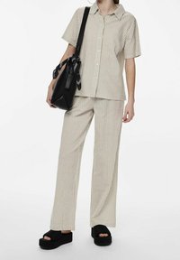 Striped, button-up shirt in beige and white paired with matching wide-leg pants. Black platform sandals and a black bag with a scarf accent.