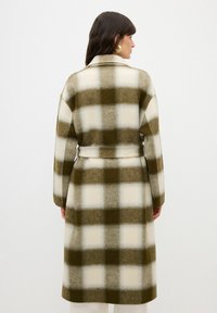 Cappotto lungo a quadri con motivo a scacchi verde e bianco. Realizzato in tessuto morbido, con vita a cintura e maniche larghe.