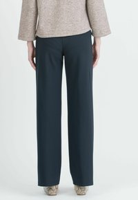 Laivansinisiä leveälahkeisia housuja, jotka on valmistettu sileästä kankaasta. Housuissa on muotoiltu istuvuus ja siisti järkätty helma. Mallilla on päällään vaaleansävyiset teksturoidut kengät.