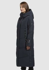 Long dark blue puffer coat with a hood, quilted design, side zip pockets, and button accents along the hem. Smooth texture.