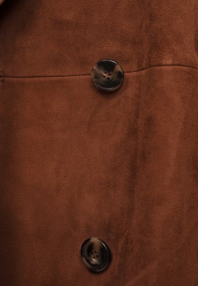 Καφέ σουέτ ύφασμα με δύο μεγάλα γυαλιστερά σκουρόχρωμα καφέ κουμπιά ραμμένα κάθετα σε μια ραφή.