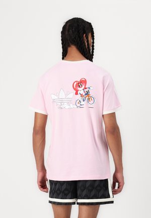 T-shirt en coton rose clair présentant un graphisme d'un personnage de dessin animé à vélo, avec une bordure blanche autour de l'encolure et des manches.