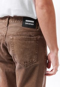 Hnědé džínsy z denimu mají texturovanou látku, nášivku značky "DRDENIM" a klasicky tvarovanou zadní kapsu.
