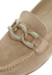 Mocassino in suede beige con un accento a catena oro e bianco sporco sulla parte superiore. La scarpa presenta cuciture visibili e un interno morbido e liscio.