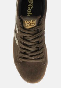 Sneaker in suede marrone con strisce bianche, punta rotonda e lacci marroni. Presenta un'etichetta con logo dorato con design della Union Jack sulla linguetta.