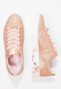 Las zapatillas de deporte con purpurina en oro rosa presentan un acabado suave, cordones de cinta y un diseño floral en la suela. Suela de goma blanca e interior acolchado.