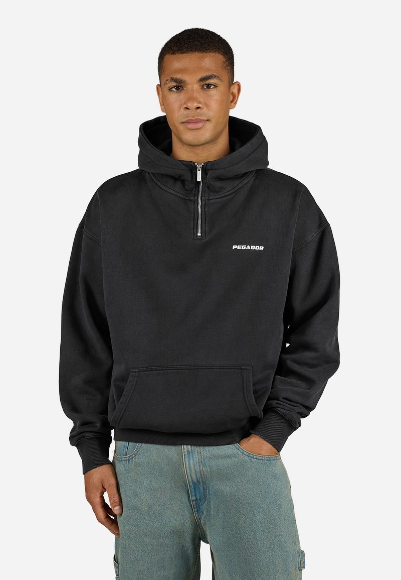 Zwarte rits hoodie met een kangoeroezak en een wit logo op de borst, gemaakt van een zachte, gestructureerde stof.