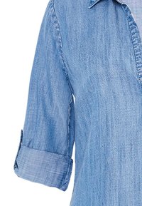 Světle modrá denimová košile s límečkem, vyhrnutými rukávy a texturovaným povrchem. Obsahuje švy podél zapínání a manžet.