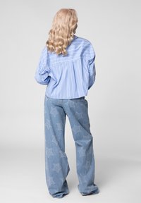 Lichtblauw gestreept shirt met een losse pasvorm, gecombineerd met denim broeken met wijde pijpen, versierd met sterrenpatronen in een lichter blauw.