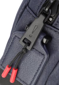 Primo piano di una borsa in tessuto blu navy, con una zip nera e un tirante con dettagli rossi, che mette in evidenza il materiale testurizzato e i dettagli di cucitura rinforzata.
