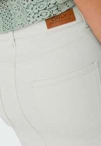 Jeans de denim blanco con detalles de costura sutiles y una etiqueta similar a cuero que dice "ONLY". Diseño visible del bolsillo trasero.