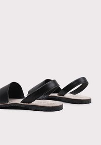 Sandalias de cuero negro con suela plana, diseño de punta abierta y dos tiras minimalistas. Suela de goma texturizada con detalle de costura.