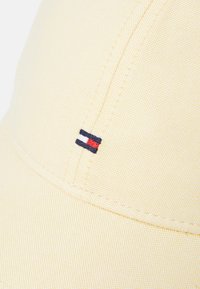 Yellow baseball cap made of textured fabric, featuring a small embroidered logo with red, white, and navy elements on the side.