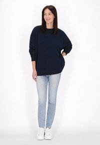 Námořnická modrá oversized mikina s kulatým výstřihem a dlouhými rukávy, kombinovaná se světle modrými úzkými džíny a bílými teniskami.