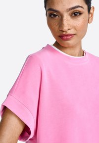 Roze oversized T-shirt van zacht materiaal met een ronde halslijn en opgerolde korte mouwen, met een gladde textuur en een minimalistisch ontwerp.