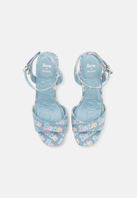 Sandales bleues avec des lettres multicolores "Barbie" sur les sangles, présentant un design à lanière arrière et une fermeture à boucle. Semelle lisse et texturée.