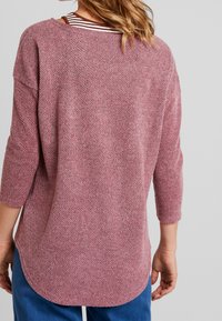 Oversized gebreide top in gedempt roze, met een textuurpatroon, driekwartmouwen en een afgeronde zoom. Gestreept ondershirt zichtbaar bij de hals.