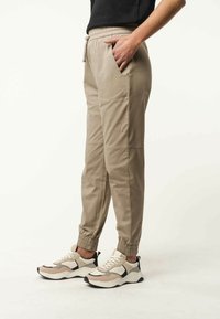 Beige afgeknotte broek met een elastische tailleband, zijzakken en elastische boorden; gecombineerd met chunky sneakers in beige en witte tinten.