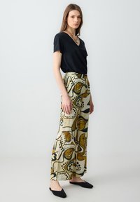 Haut noir à col en V associé à un pantalon large taille haute avec une base crème et des motifs abstraits marron et bleu. Chaussures noires à enfiler.
