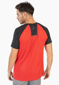 Camiseta deportiva roja y negra de manga corta, con rayas texturizadas en el cuerpo y un yugo negro. Presenta un pequeño logo en la parte posterior.