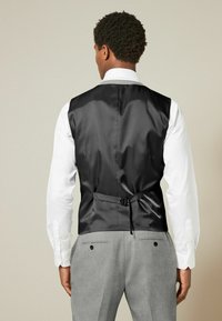 Black satin vest with a fitted design, adjustable back strap, and a contrast white dress shirt. Gray trousers visible below.