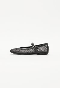 Black flat shoe with a rounded toe, featuring a mesh upper with polka dots and a strap with a buckle on the side.